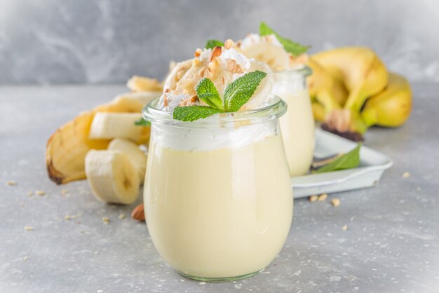 Pudim de banana fresca no café da manhã, iogurte de banana. sobremesa doce em copos com rodelas de banana e nozes, lanche vegetariano cru