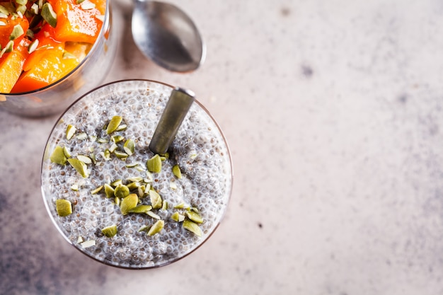 Pudim de chia com caqui e sementes de abóbora em copos, fundo cinza, vista superior. conceito de comida vegan.