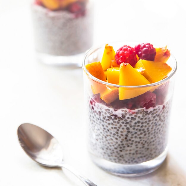 Pudim de Chia em leite de coco com framboesas e pêssego em potes de vidro em uma mesa branca