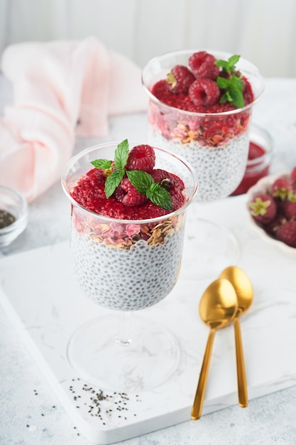 Pudim de chia Pudim de chia de baunilha saudável em vidro com framboesas frescas e hortelã em fundo branco Café da manhã saudável vegan