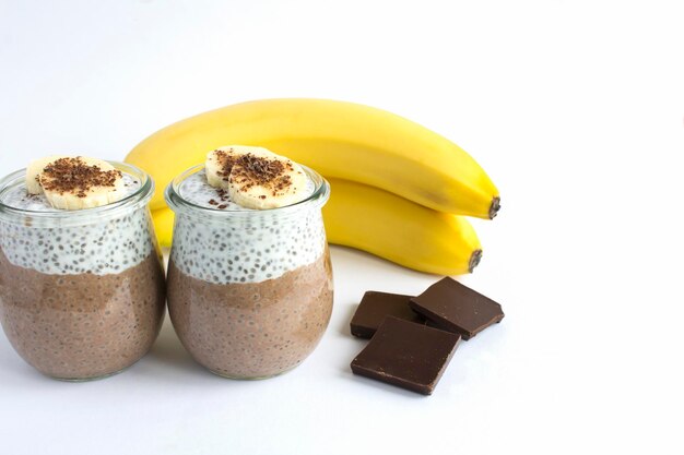 Pudim de chocolate com semente de chia e banana nos frascos de vidro no fundo branco copie o espaço