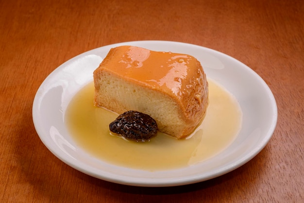 Pudim de leite com calda de ameixa em chapa branca na mesa de madeira