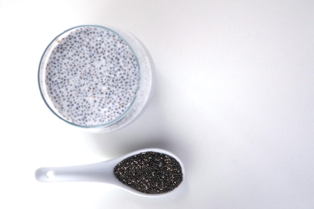 Pudim de leite com sementes de chia e uma colher de cerâmica com sementes de chia secas em fundo branco