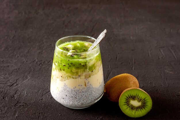 Pudim de semente de chia com kiwi, banana e manga. Café da manhã desintoxicante de saúde em copos em concreto preto