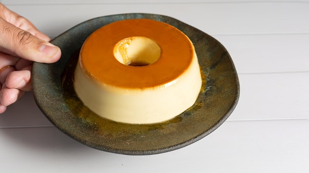 Pudim tradicional de huevos o pudín de postre brasileño o también conocido como vista superior flan sobre la mesa con el brazo masculino poniendo el plato oscuro sobre la mesa