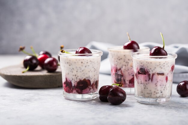 Pudín de chía con cerezas, yogur natural, en un vaso sobre una superficie gris