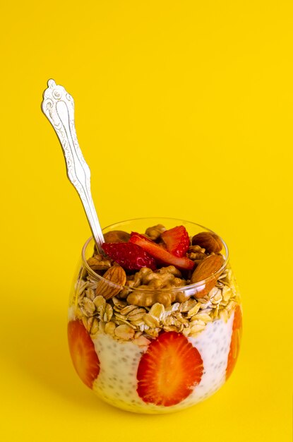 Pudín de chia con fresas, avena y nueces en un vaso sobre amarillo