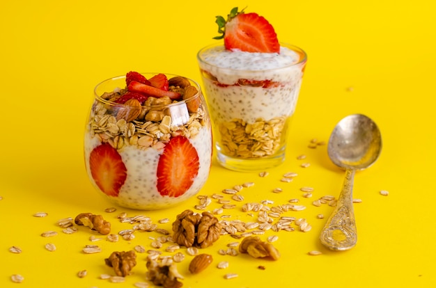 Pudín de chia con fresas, avena y nueces en un vaso sobre amarillo