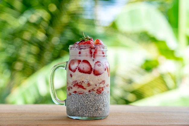 Pudín de chía con leche de almendras con fresas rojas frescas, bayas de goji y copos de avena en una taza de tarro de vidrio Desayuno crudo vegano Semillas de chía y frutas frescas cortadas y postre de bayas de cerca