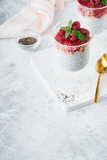Pudín de chía Pudín de chía de vainilla saludable en vaso con frambuesas frescas y menta sobre fondo blanco Desayuno vegano saludable