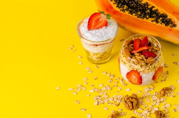 Pudín de yogur de chía con fresas, avena y nueces en un vaso sobre amarillo