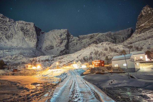 Pueblo colorido noruego rodeado de montañas nevadas con estrellas en la noche