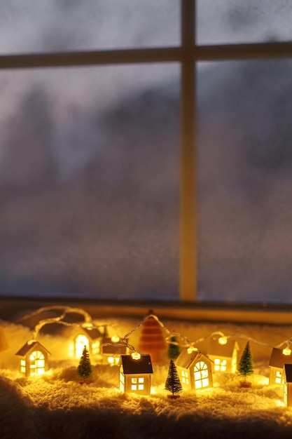 Pueblo invernal en miniatura atmosférico Elegantes y lindas casitas brillantes y árboles de Navidad sobre una suave manta nevada en la sala de noche Fondo navideño de higiene Felices fiestas
