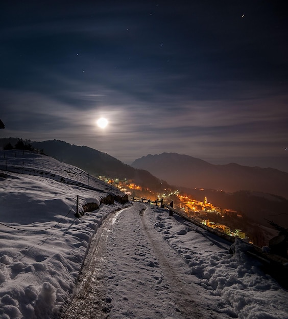 Pueblo de montaña cubierto de nieve en la noche con la luna