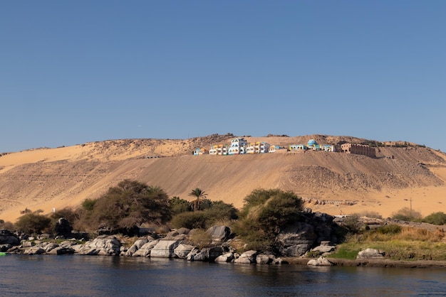 Pueblo nubio tradicional en la cima de la colina de arena en la orilla del río Nilo con vegetación y cielo azul claro