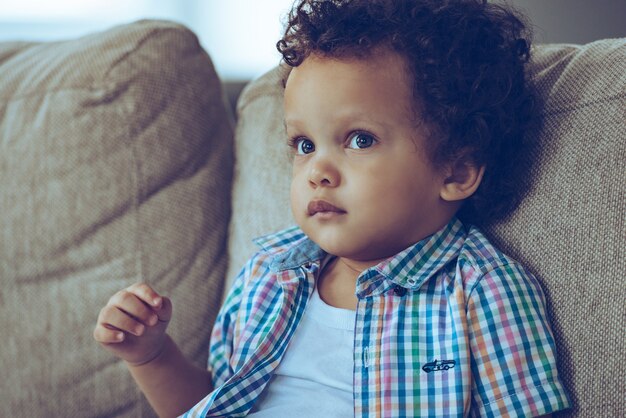 Puedes ahogarte en sus ojos. Retrato de niño africano mirando a otro lado mientras está sentado en el sofá en casa