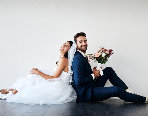 Puedes apoyarte en mí cualquier día Foto de estudio de una pareja joven recién casada sentada espalda con espalda en el suelo contra un fondo gris