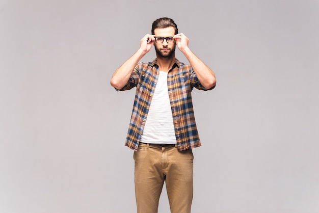 Puedo verte claramente. Foto de estudio de apuesto joven en ropa casual ajustando sus anteojos y mirando a la cámara