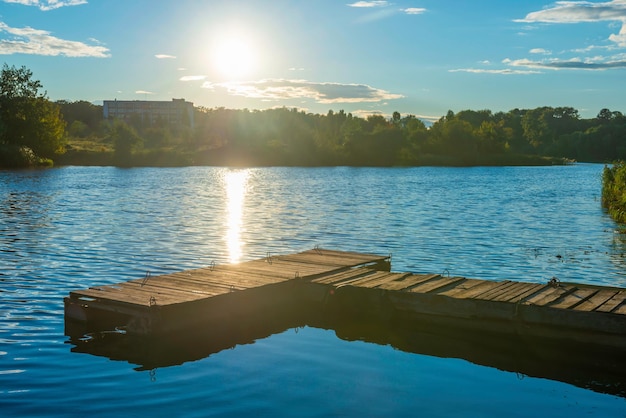 Puente de amarre de madera al atardecer del agua con reflejo del sol en el agua