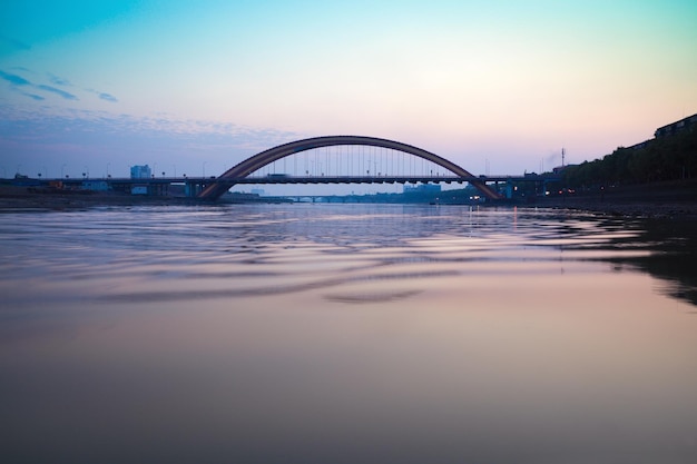 Puente de arco de carretera al atardecer con olas en el río