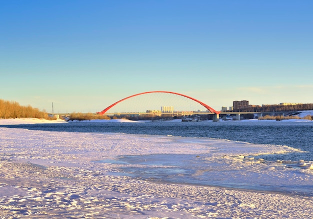 Puente de arco en el puente Bugrinsky del río Ob en la orilla nevada en la gran ciudad en primavera