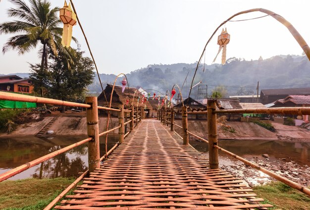 Foto puente de bambú a través del pequeño río con el sol