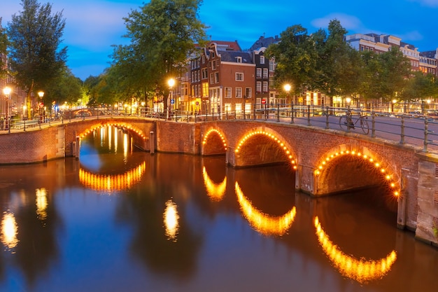 Puente del canal de Amsterdam y casas típicas, barcos y bicicletas durante la hora azul del crepúsculo vespertino