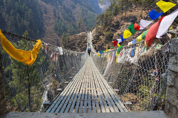 Puente colgante sobre el precipicio con coloridas banderas en nepal en verdes bosques y colinas.