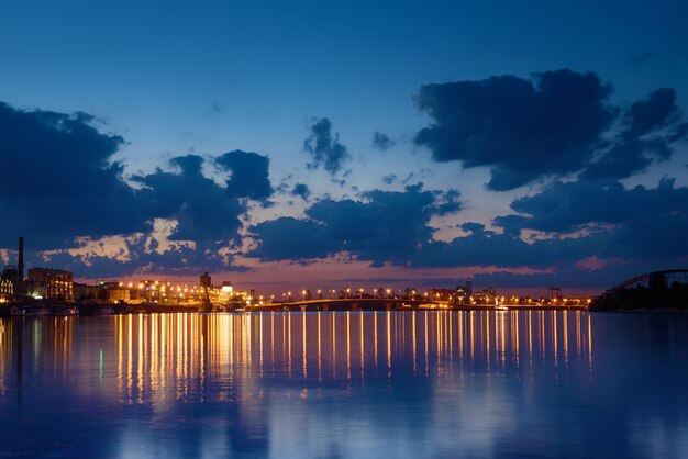 Puente de La Habana en Kiev por la noche con iluminación colorida, hermosas nubes y reflejo en el río Dnieper. Gran angular