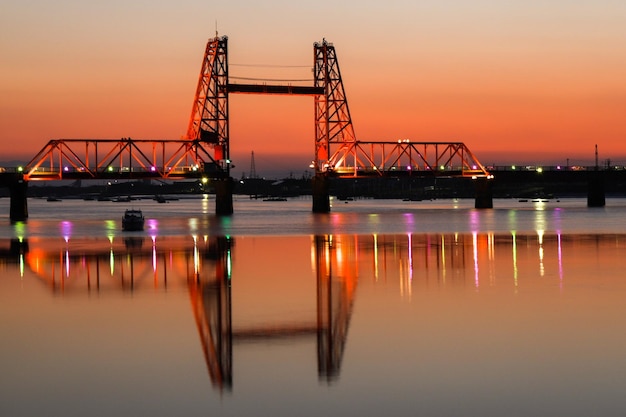 Foto puente iluminado sobre el río contra el cielo durante la puesta de sol