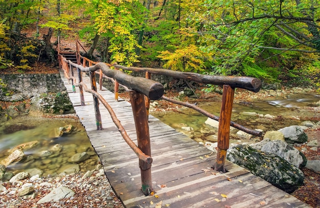 Foto puente de madera en el bosque de otoño. cruzando el pequeño río hacia el gran cañón de crimea