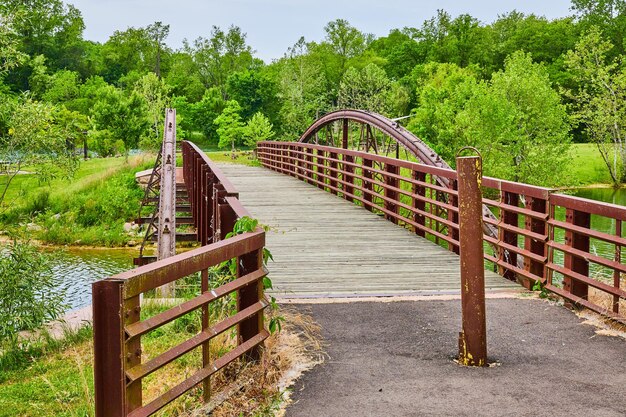 Puente peatonal de metal de hierro oxidado con pintura amarilla en el poste que conduce a los gansos canadienses en la hierba