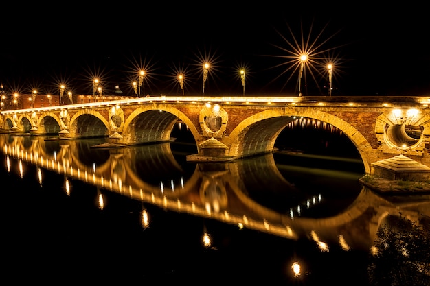 Puente Pont Neuf iluminado por la noche. Una pequeña parte de la iluminación está rota. Hermoso reflejo en el río Garona. Toulouse, Francia