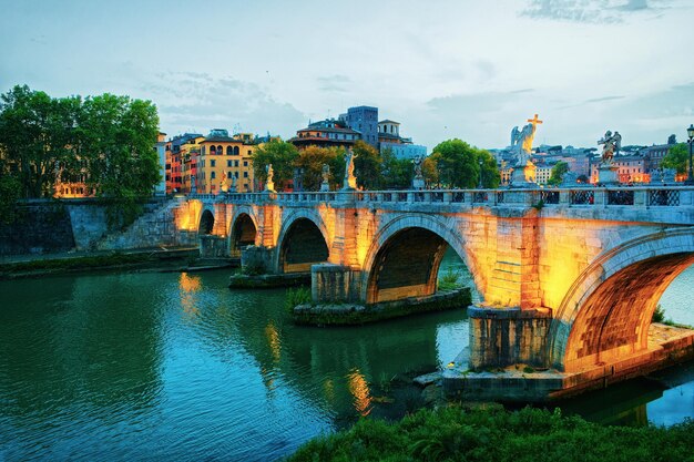 Puente Ponte Sant Angelo sobre el río Tíber, en Roma en Italia. Es también llamado como el Puente de Adriano. Iluminado tarde en la noche