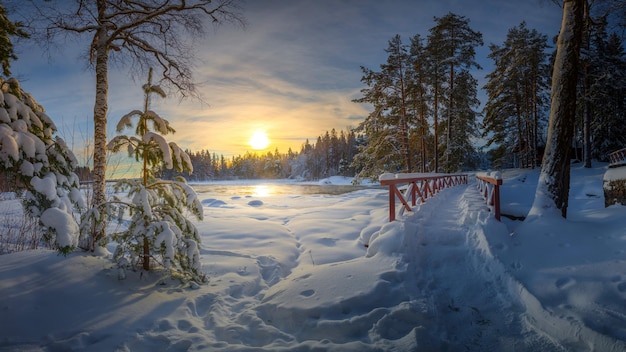 un puente rojo está en la nieve con el sol poniéndose detrás de él