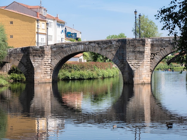 Puente romano de piedra situado en la ciudad gallega de Monforte de Lemos sobre el río Cabe en un día soleado que proyecta su reflejo en el agua que fluye