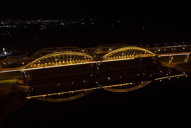 Puentes de luces brillantes con arcos ciudad nocturna Un puente de carretera a través del río tomado de un avión no tripulado