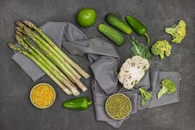 Püree und Bulgur in Schüsseln. Spargel, Blumenkohlhälfte, Brokkoli auf grauer Serviette. Gurken und Paprika auf dem Tisch. Schwarzer Hintergrund. Flach legen