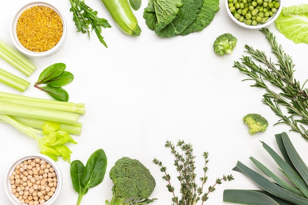 Puerro, repollo, tallos de apio, cereales y guisantes verdes en tazones, ramitas de tomillo y romero alrededor de los bordes del fondo. Copie el espacio. Endecha plana. Fondo blanco