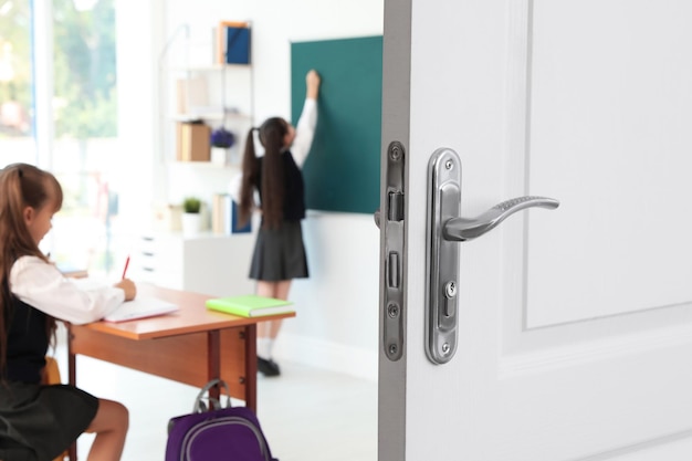 Puerta de madera abierta al aula moderna con estudiantes