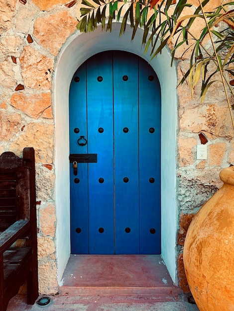 Puerta de madera azul con cerrojo antiguo junto a silla antigua y maceta amarilla grande