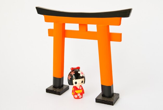 Puerta torii con muñecas japonesas sobre fondo blanco.