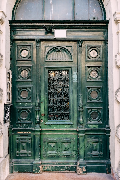 Puertas de madera verde tallada con pilares de vidrio y estrecho exterior en la fachada de un edificio en un