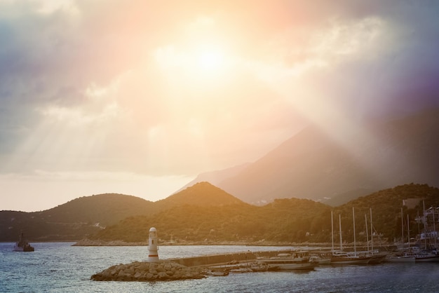 Puerto marítimo y faro en el fondo de las montañas al amanecer o al atardecer