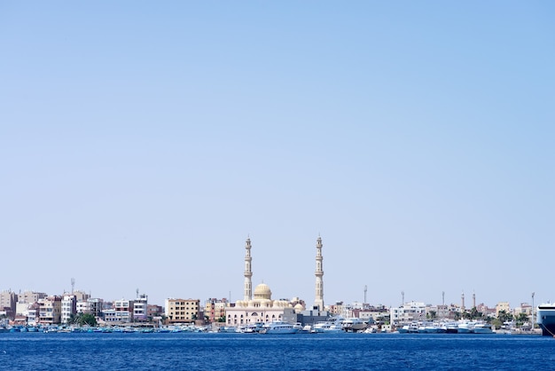 Puerto marítimo con terraplén de la ciudad de piedra con lanchas rápidas estacionadas y la mezquita de Hurghada