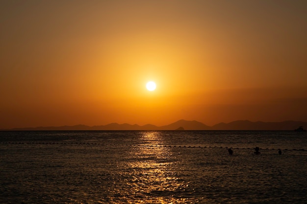 Puesta de sol dorada sobre las líneas de la montaña del mar en el fondo gente nadando en el agua