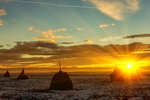 Puesta de sol de invierno sobre un campo con nieve y pajares