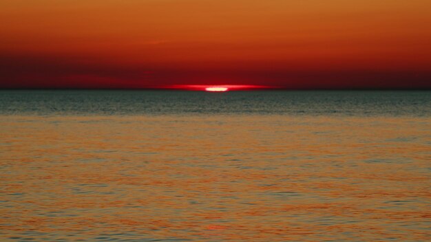 La puesta de sol en la línea del mar con el agua oscura ondulante del océano sol en el mar con colores naranja y rojo lento