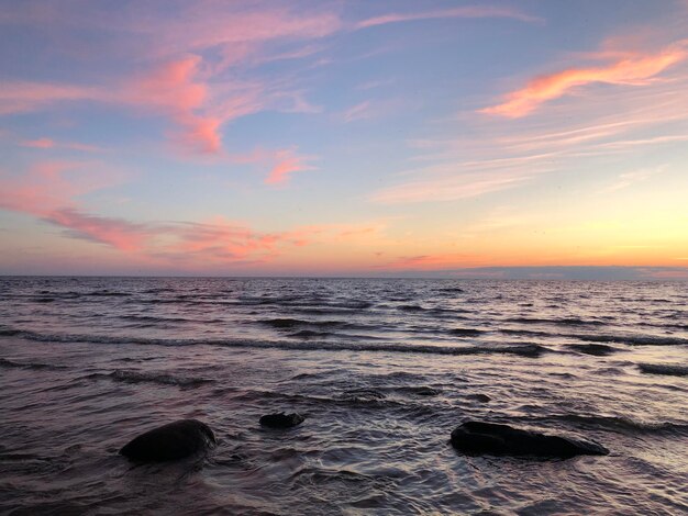 La puesta de sol en el mar con un hermoso cielo de colores grandes piedras oscuras y aguas onduladas