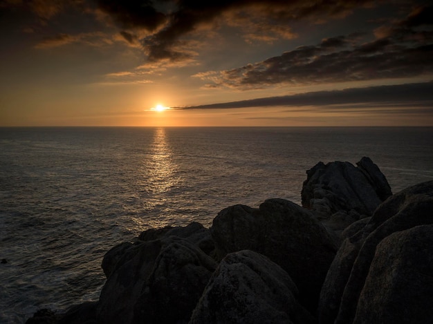 Puesta de sol con nubes sobre el mar con rocas en primer plano